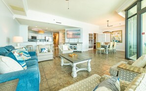 A spacious living room with a sofa, a coffee table, and a dining area with chairs and a table. - Phoenix West 603 3 Bedroom Condo (Orange Beach)