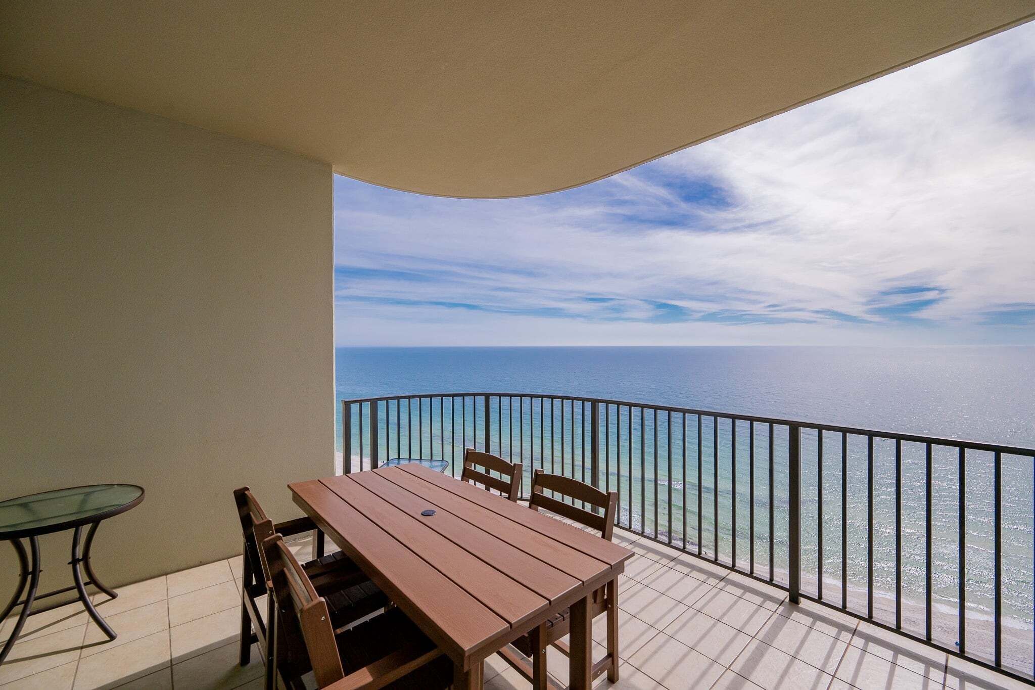 A balcony with a table and chairs, a glass table, and a view of the sea.