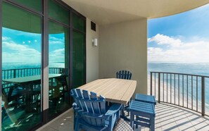 A balcony with a wooden table and chairs, a glass door, and a view of the ocean. - Phoenix West 2203 3 Bedroom Condo (Orange Beach)
