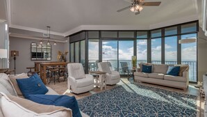 A spacious living room with a large window, a ceiling fan, and a dining area. - Phoenix West 2203 3 Bedroom Condo (Orange Beach)