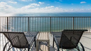 A balcony with two wicker chairs and a small table, overlooking a calm sea and clear sky. - Phoenix West 2203 3 Bedroom Condo (Orange Beach)