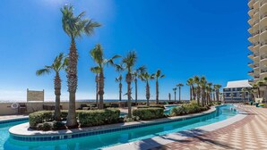 A swimming pool with palm trees, a clear sky, and a building with balconies. - Phoenix West 2203 3 Bedroom Condo (Orange Beach)