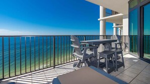 A balcony with a view of the ocean, a table, and chairs. - The Oasis 1607 Formerly Phoenix West Ii 1607 3 Bedroom Condo (Orange Beach)