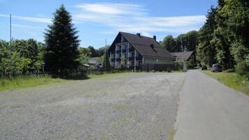 A two-story building with a sloped roof, a visible balcony on the second floor, and a gravel driveway leading to a paved road.