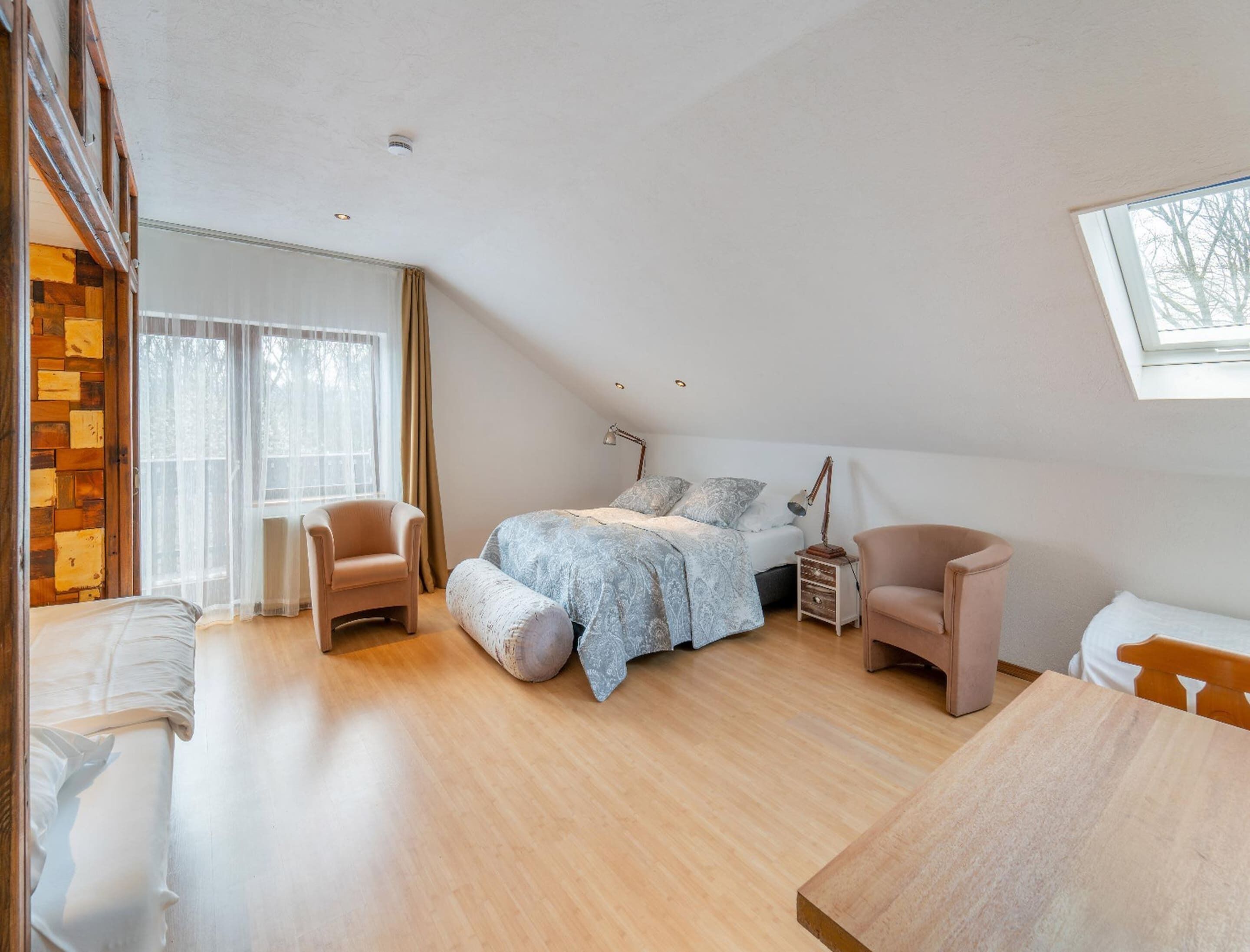 A bedroom with a bed, two chairs, a wooden table, and a window.