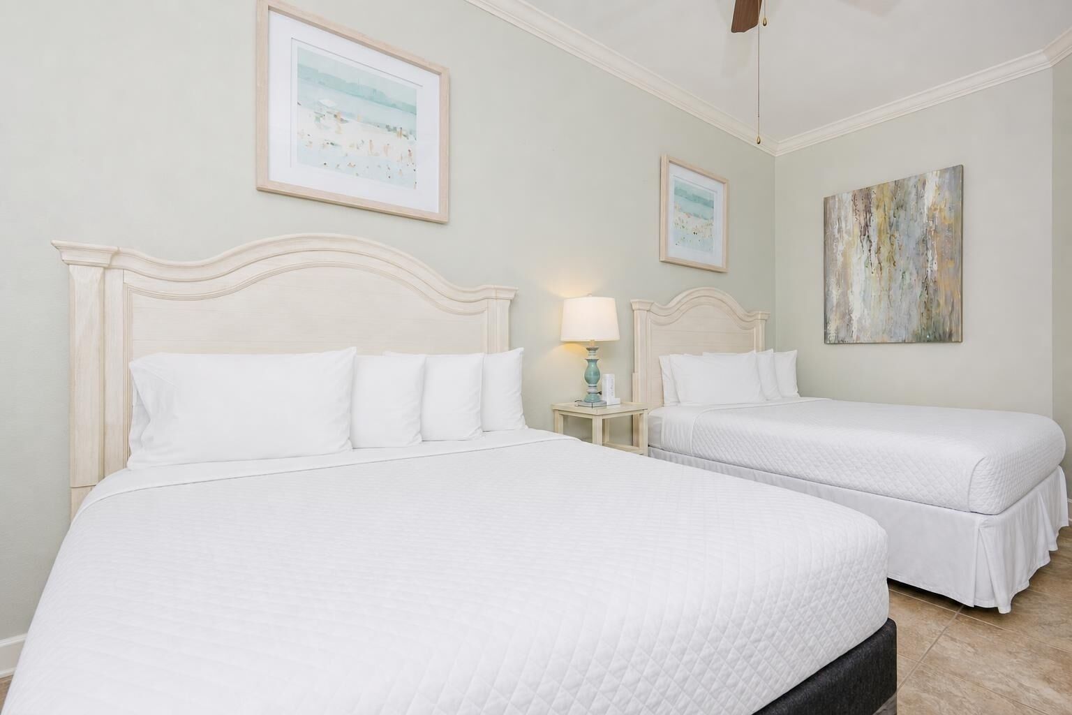 Una camera d'albergo con due letti, un comodino con una lampada e opere d'arte alle pareti.