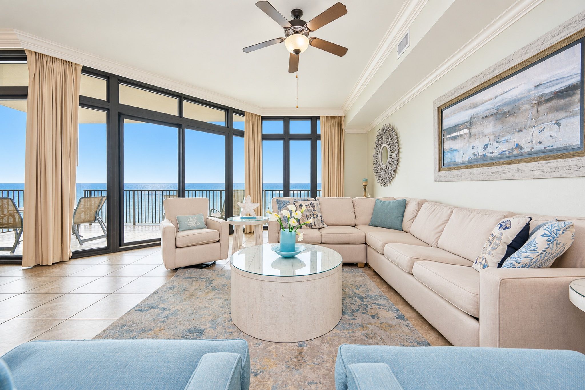 A spacious living room with a large window, a ceiling fan, and a view of the ocean.