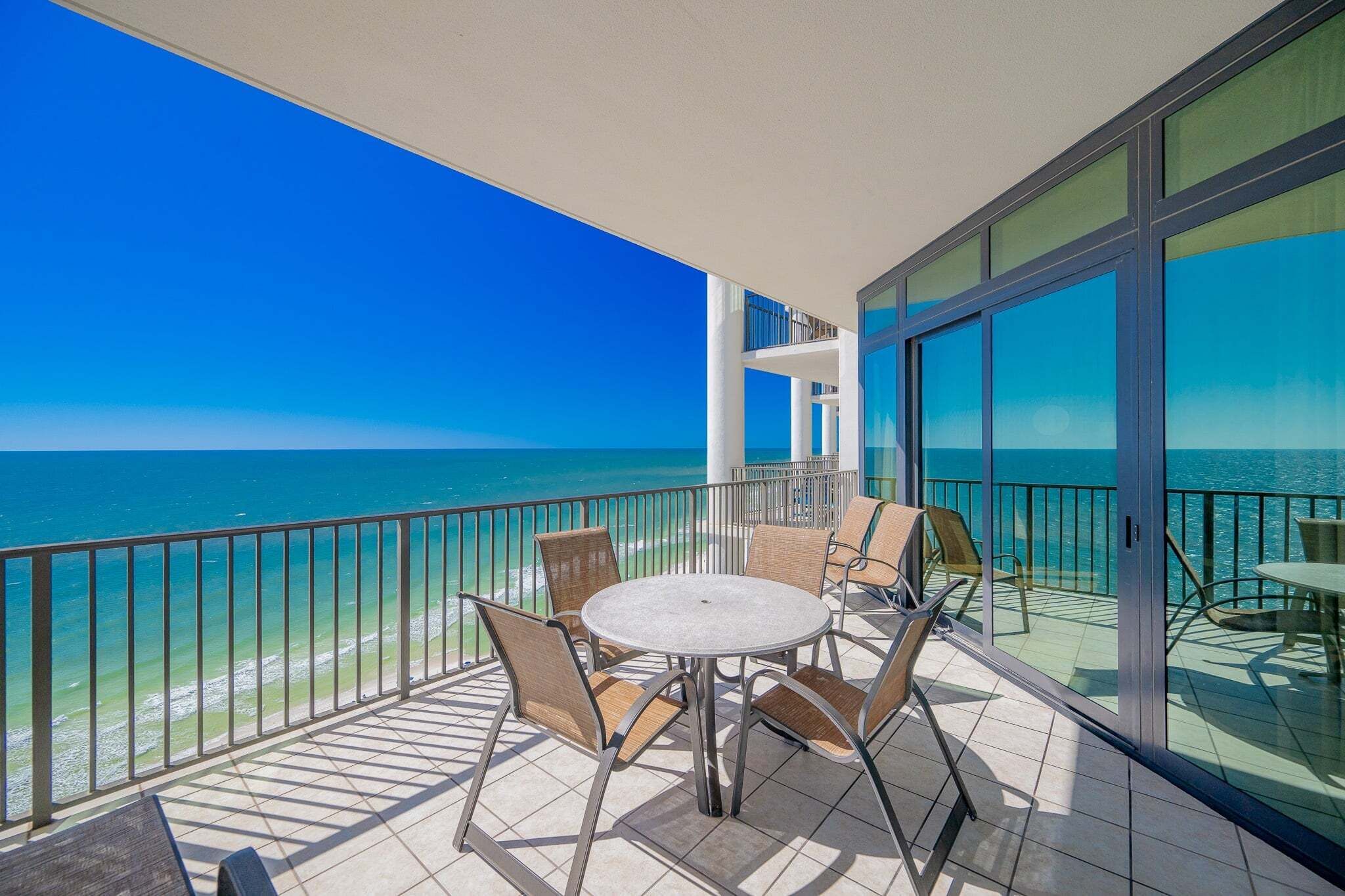 Un balcon avec une table ronde et des chaises, donnant sur une plage et l’océan.