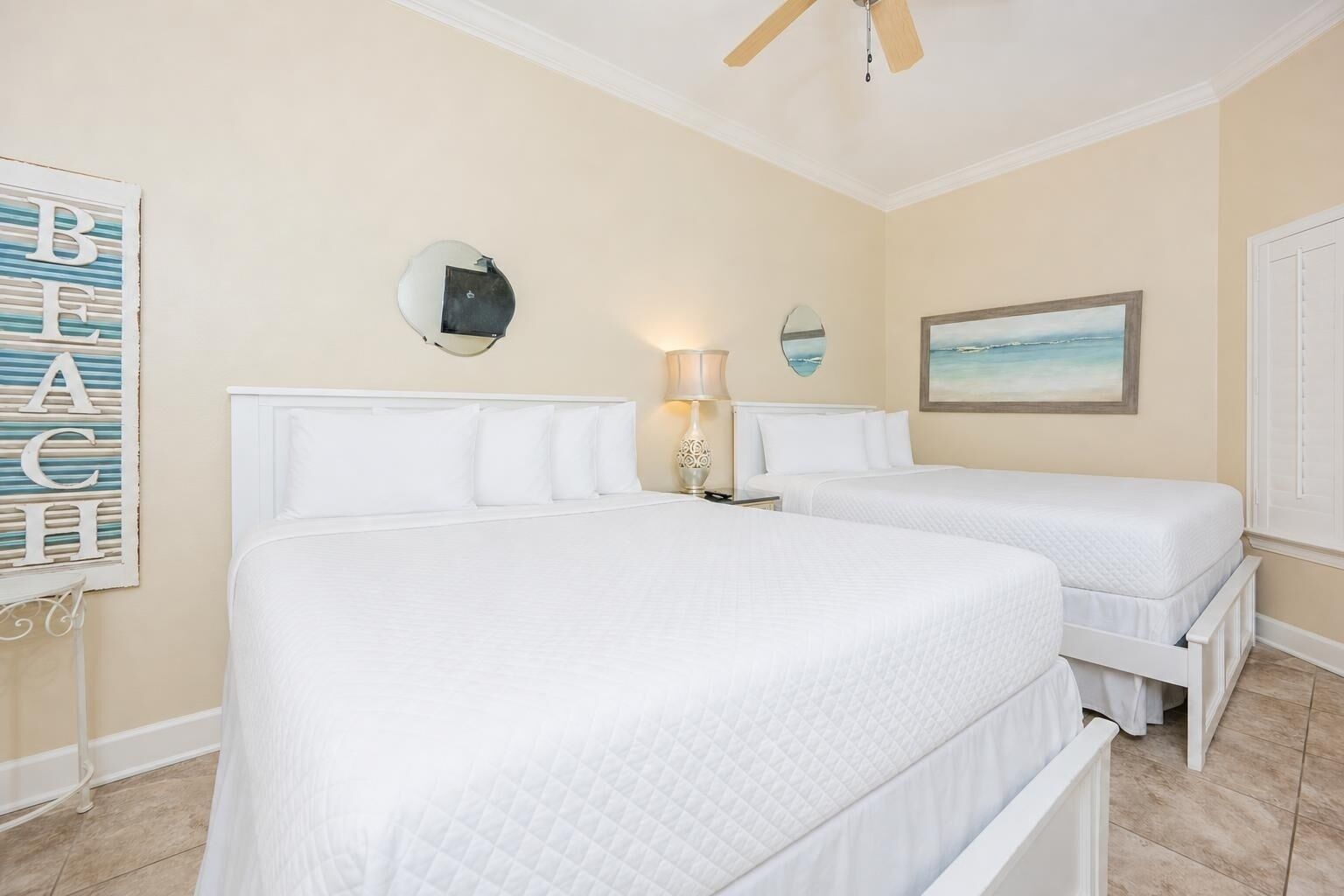Une chambre d’hôtel avec deux lits, un ventilateur de plafond, un tableau et un miroir décoratif.