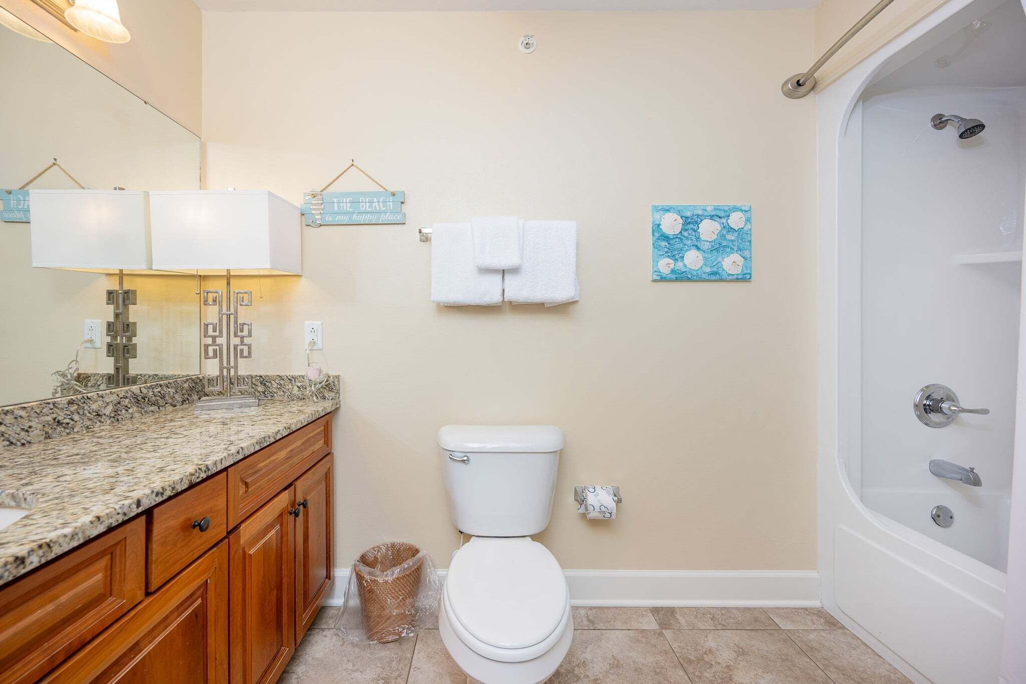 A bathroom with a toilet, a sink with a marble countertop, a shower, and a towel rack.