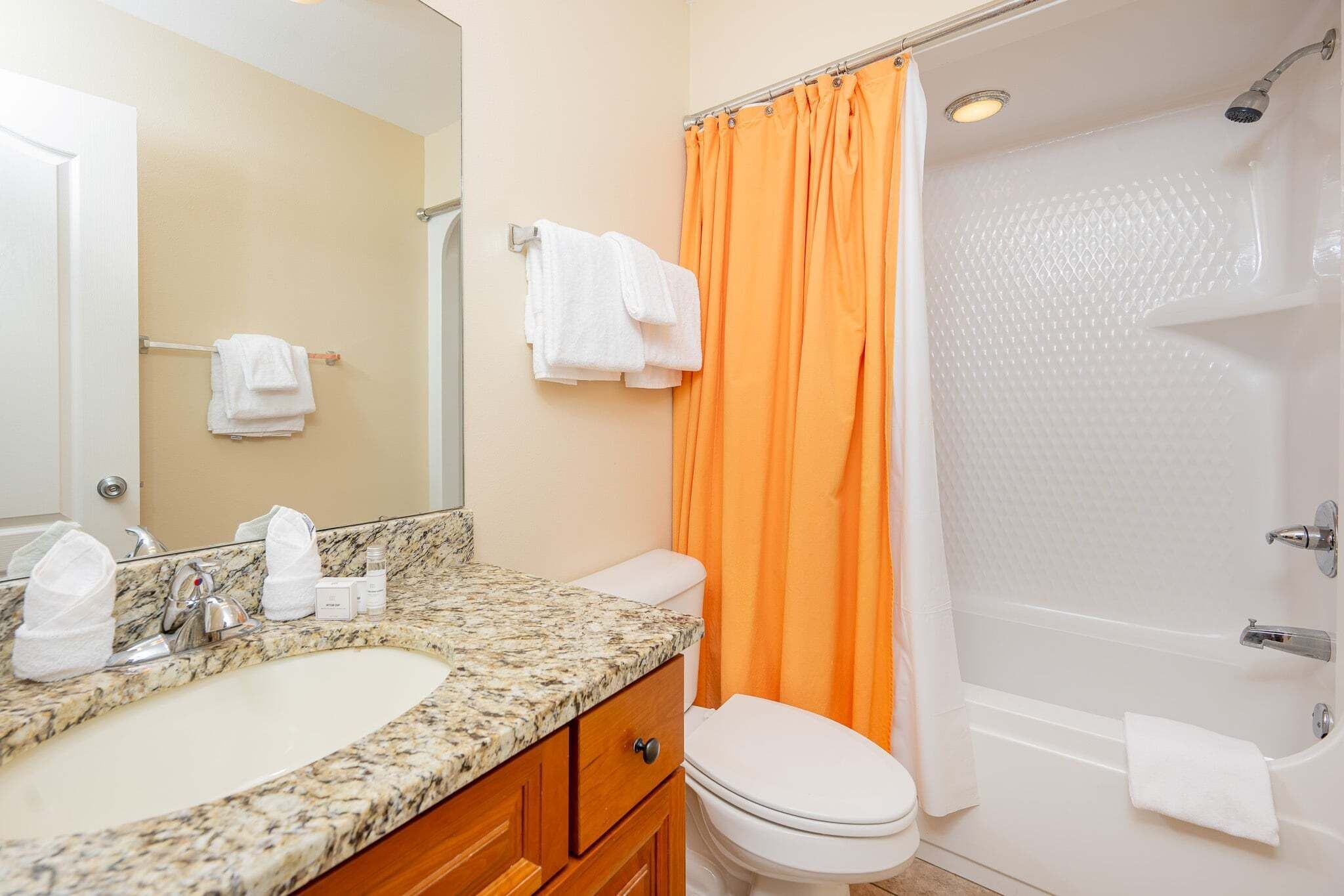 Une salle de bain avec un lavabo en marbre, des toilettes blanches et un rideau de douche orange.