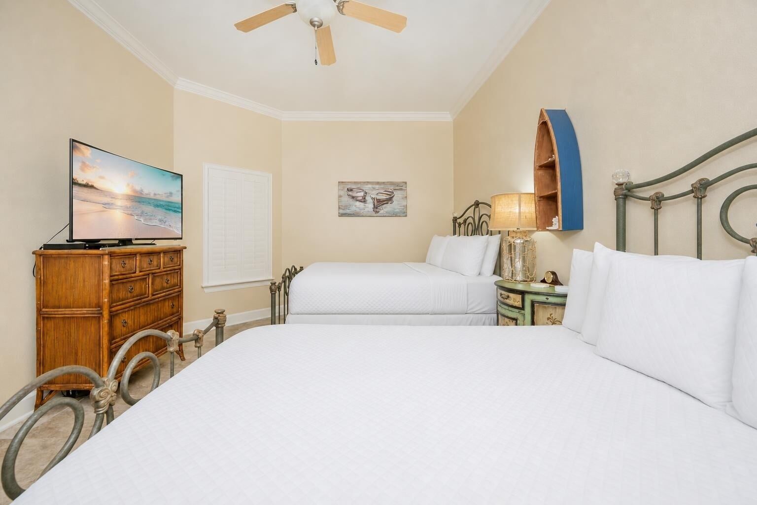 A hotel room with two beds, a television, a wooden dresser, a ceiling fan, and a painting on the wall.