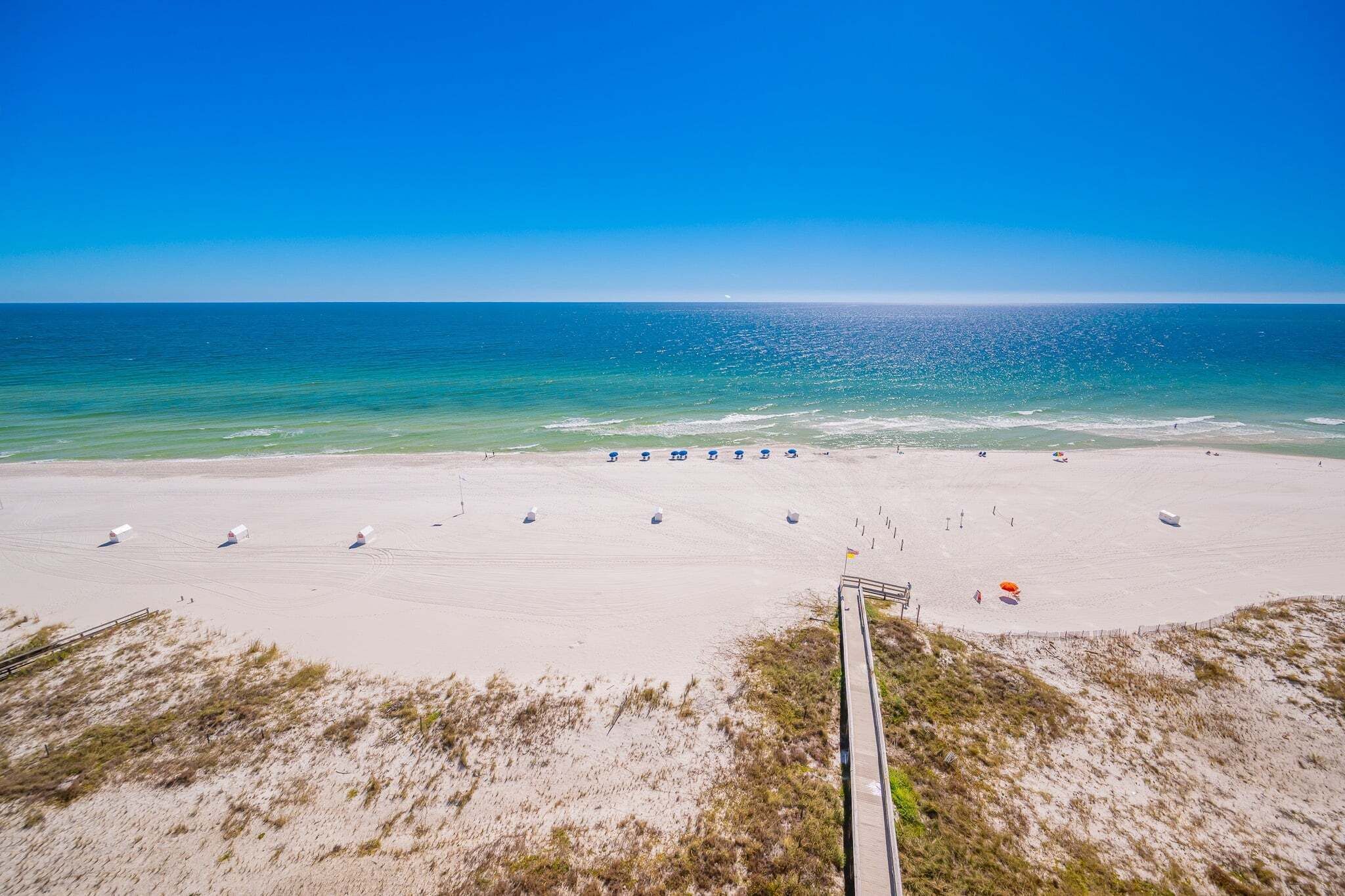 A beach with a wooden boardwalk leading to the water, sandy beach, and umbrellas.