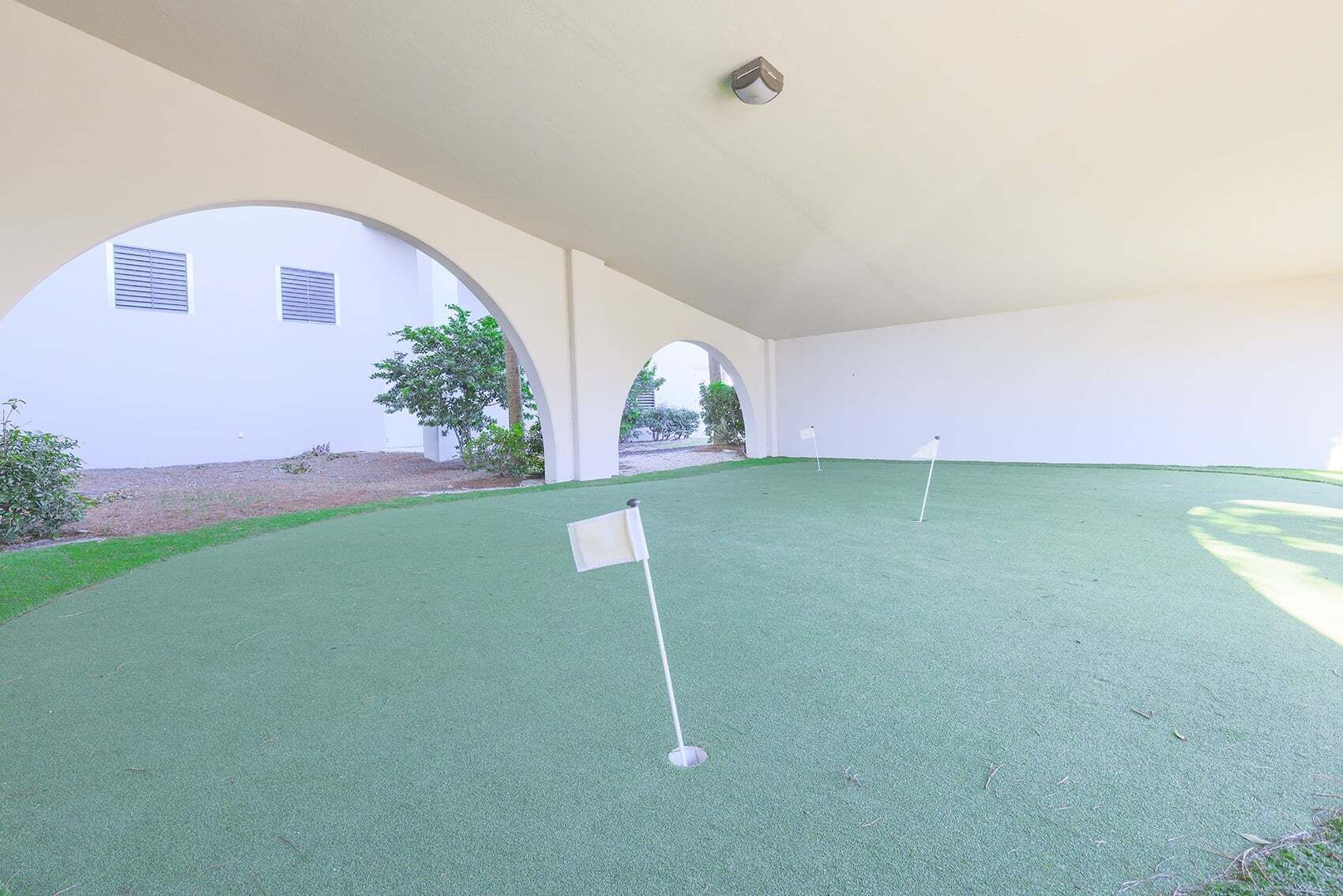 Un área de práctica de golf en interiores con césped artificial y banderas.
