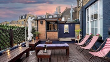 A rooftop patio with wooden furniture, a small bar area, and striped lounge chairs.