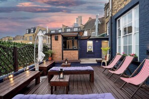 A rooftop patio with wooden furniture, a small bar area, and striped lounge chairs. - Modern Terrace Flat on Brick Lane in Shoreditch - Near Tower Bridge, London (London)
