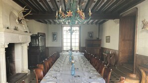 A long dining table set for a meal, with chairs on both sides, a chandelier, and a fireplace with antlers on the wall. - Chateau à 20 min du circuit des 24H (Soulitré)