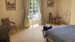 A bedroom with a bed, a chair, a table with a vase of flowers, and two framed pictures on the wall. - Chateau à 20 min du circuit des 24H (Soulitré)