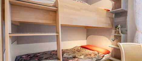 A bunk bed with a desk and chair, a shelf with books, and a window with curtains.