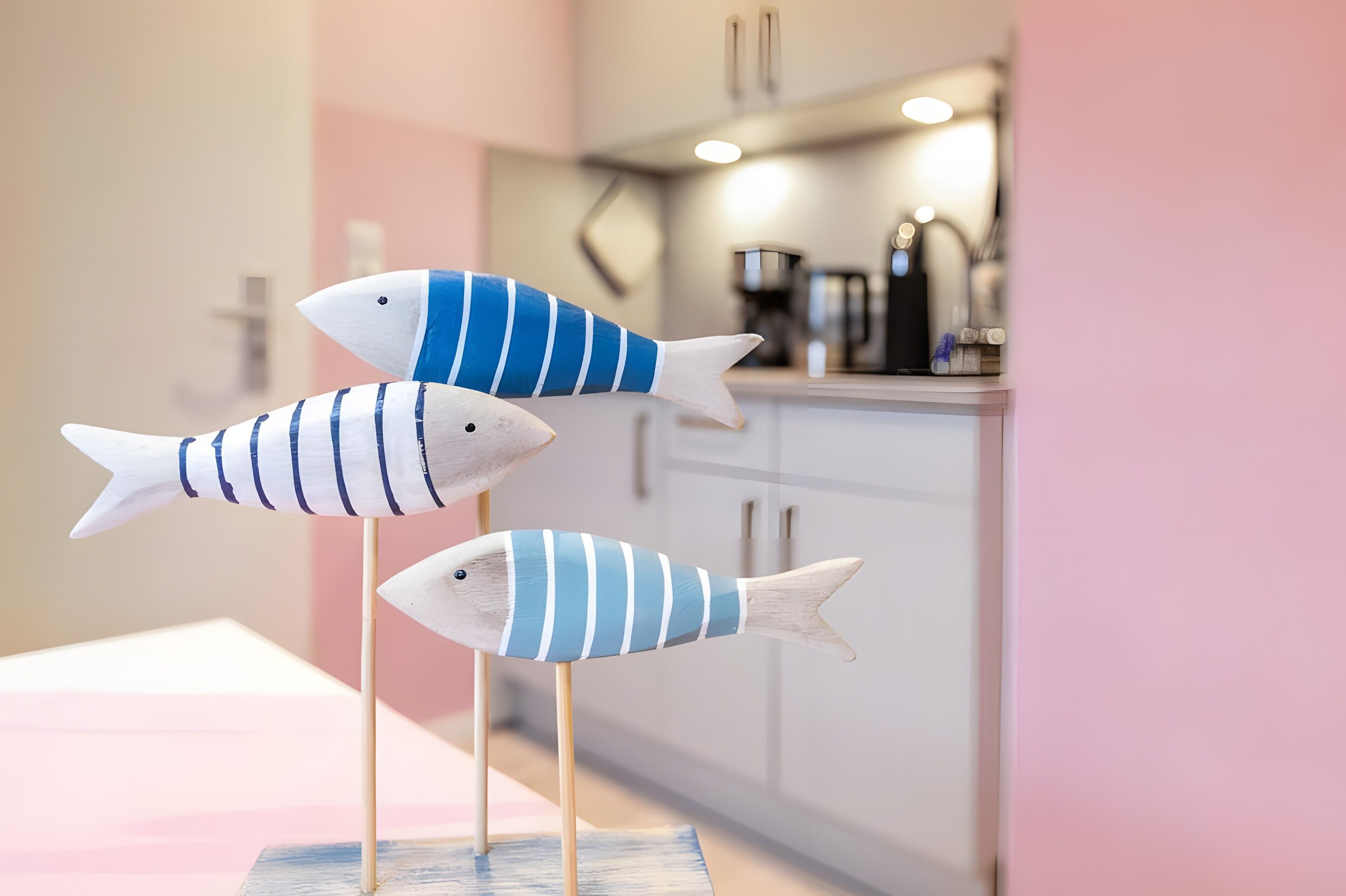 Three wooden fish on sticks in a kitchen with cabinets and a coffee machine.