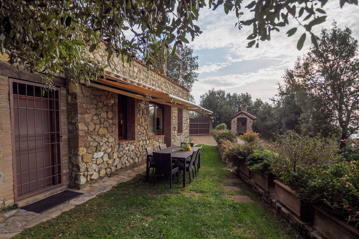 Una casa de piedra con un patio, un jardín pequeño y una pérgola de madera.