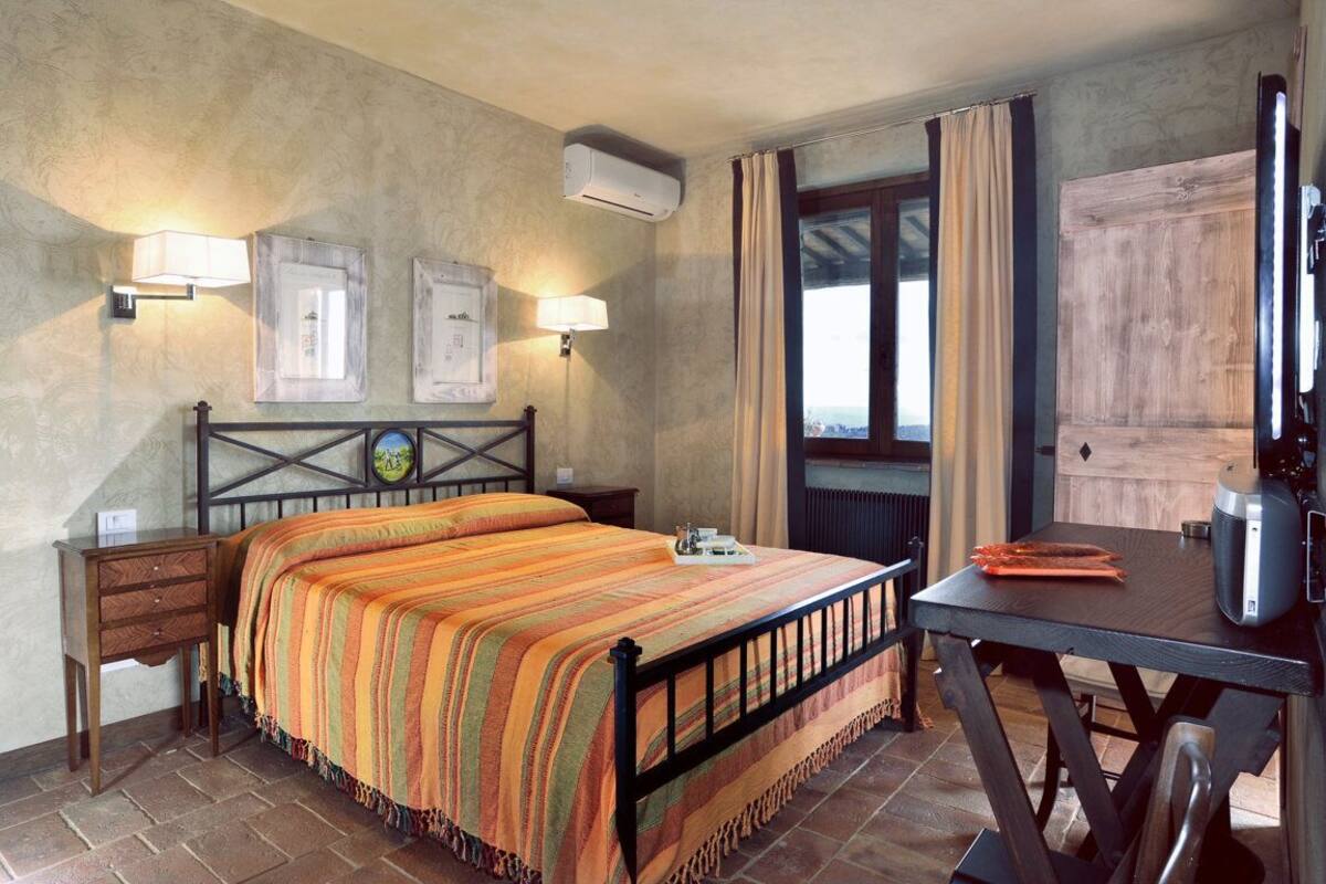 Una habitación con cama, mesita de noche, lámpara, aire acondicionado, ventana con cortinas y vistas.