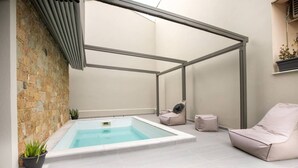 A modern indoor pool area with a stone wall, a hot tub, and two cushioned seating areas. - Villa Magdalena by RentalsPro - Nikiti Halkidiki (Νικήτη)
