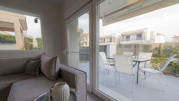 A modern living room with a sofa, a small table, and a view of the outdoor patio area. - Villa Magdalena by RentalsPro - Nikiti Halkidiki (Νικήτη)
