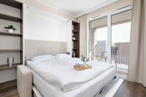 Una camera d'albergo moderna con un letto, scaffali a parete, un piccolo balcone e una porta scorrevole in vetro.