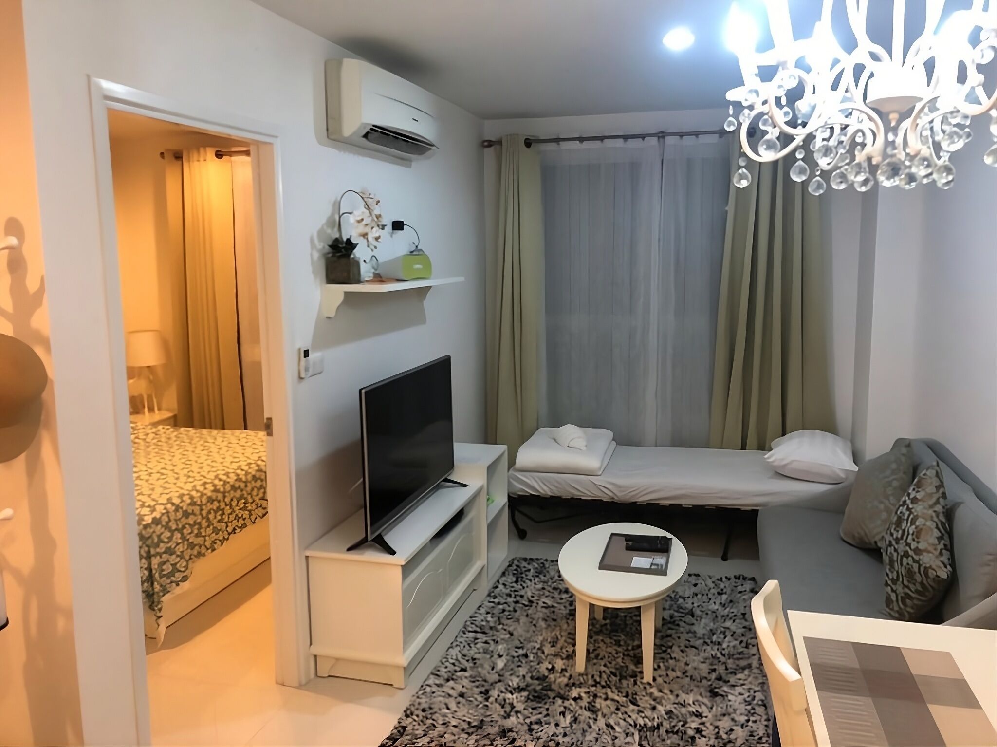 Een hotelkamer met een bed, een televisie, een tafeltje, een stoel, een bank, een kroonluchter en een airconditioner.
