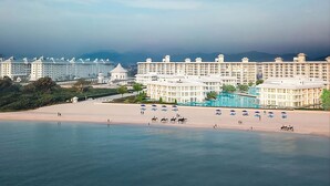 Un hotel frente al mar con varias edificaciones, una playa y una zona de piscina.