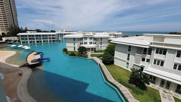 Un hotel moderno con una gran piscina, varias edificaciones y vista al océano.