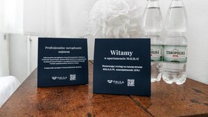 Zwei schwarze Schilder mit Text und QR-Codes, eine weiße Blume und zwei Wasserflaschen auf einer Holzoberfläche.