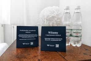 Dos carteles negros con texto y códigos QR, una flor blanca y dos botellas de agua sobre una superficie de madera.