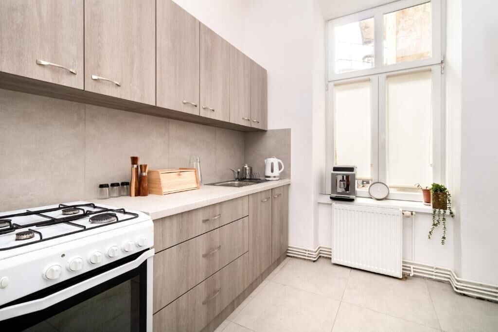 Eine moderne Küche mit Gasherd, Holzschränken, einem Fenster mit Blick und einer weißen Arbeitsplatte.