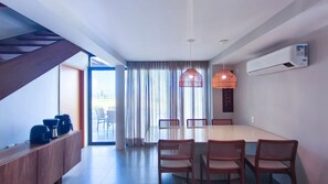 A modern dining area with a long table and wicker chairs, a staircase on the left, and an air conditioning unit on the wall. - Bangalo no Carneiros Atlantico by CTA (Tamandaré)