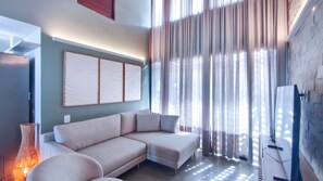 Un salón moderno con un sof á modular, un cuadro abstracto grande y vistas a través de cortinas traslúcidas.