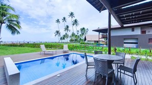 Ein Pool mit Liegestühlen und einem Tisch, umgeben von einer Holzterrasse und Palmen.