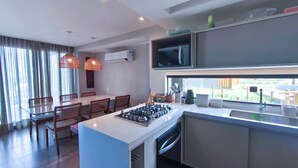A modern kitchen with a central island, dining area with chairs, and a large window. - Bangalo no Carneiros Atlantico by CTA (Tamandaré)