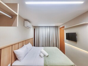 Ein Hotelzimmer mit einem Bett, einem flachbildfernseher an der Wand, einer Klimaanlage und einem Vorhang.