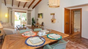 Un coin repas avec une table en bois dressée pour quatre personnes, entourée de chaises, et offrant une vue sur l’extérieur.