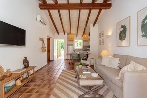 Ein geräumiges Wohnzimmer mit einer Couch, einem Couchtisch und einem Fernseher. Im Hintergrund befindet sich eine Küche mit einem Esstisch und Stühlen.
