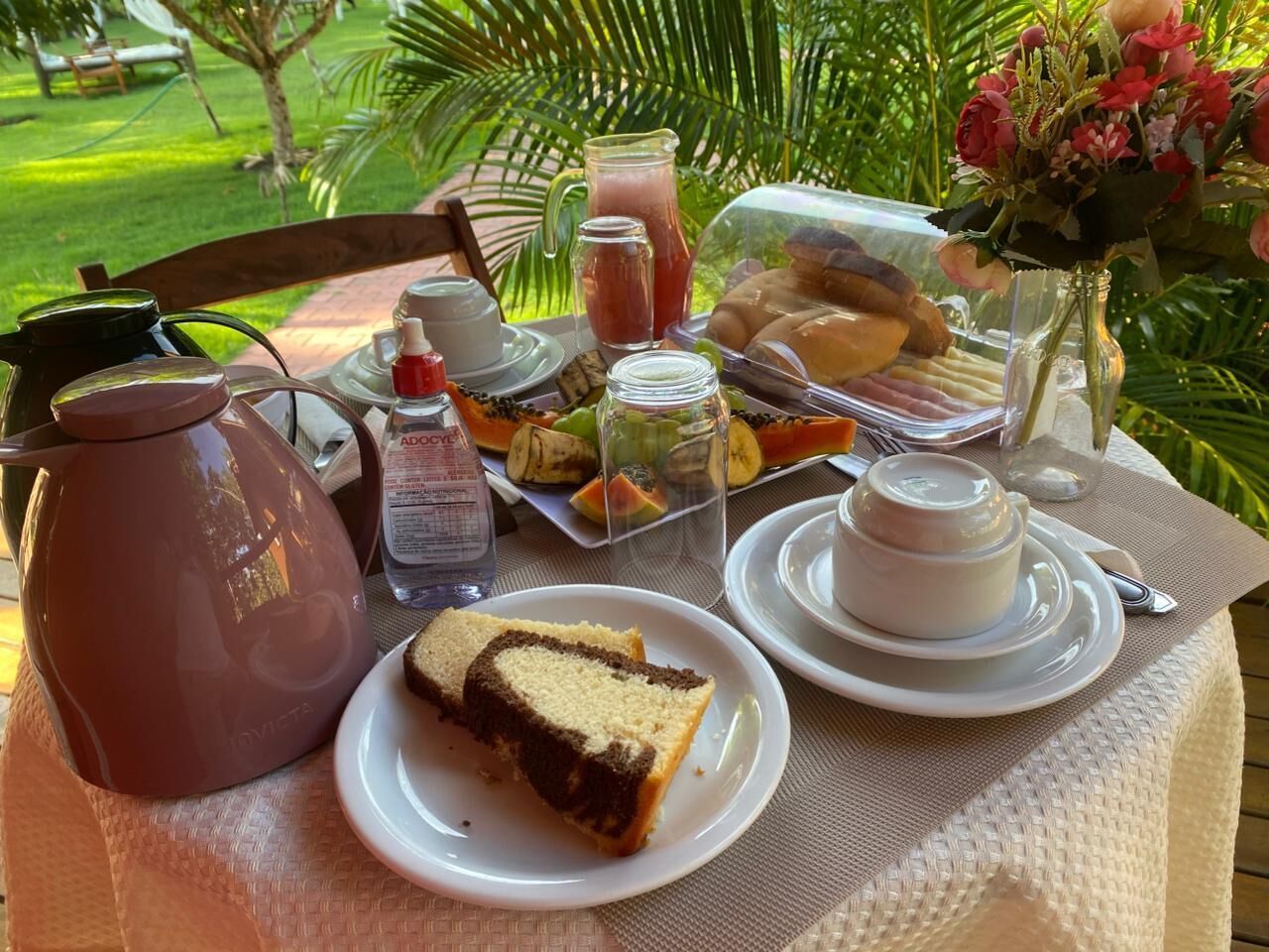 A table set with food and drinks, a pitcher, a vase with flowers, and a view of a garden.