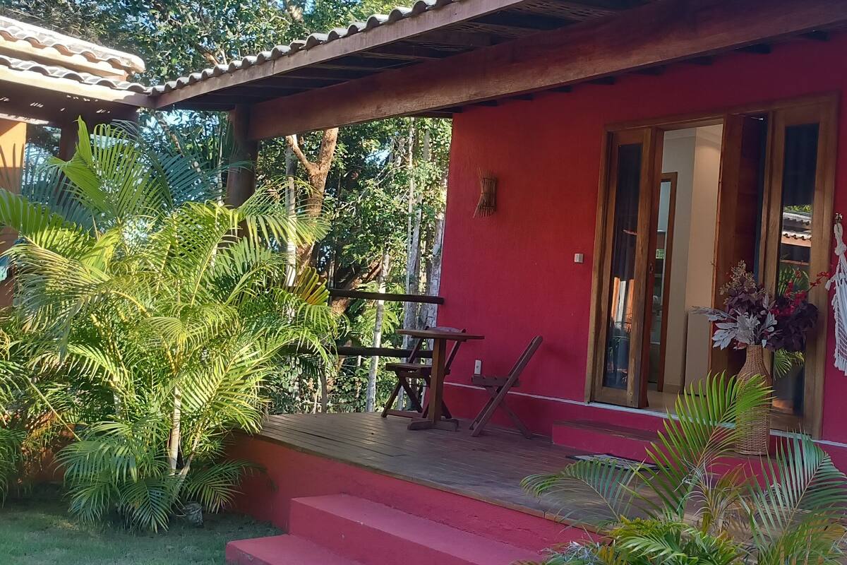 Un edificio rojo con un porche de madera, una hamaca y una mesa con sillas.