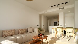Een moderne woonkamer met een bank, salontafel en stoelen, een keuken op de achtergrond, en een eethoek met een tafel en stoelen.