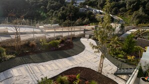 Een aangelegde buitenruimte met een kronkelend pad, een kleine brug en een omheinde tuin.