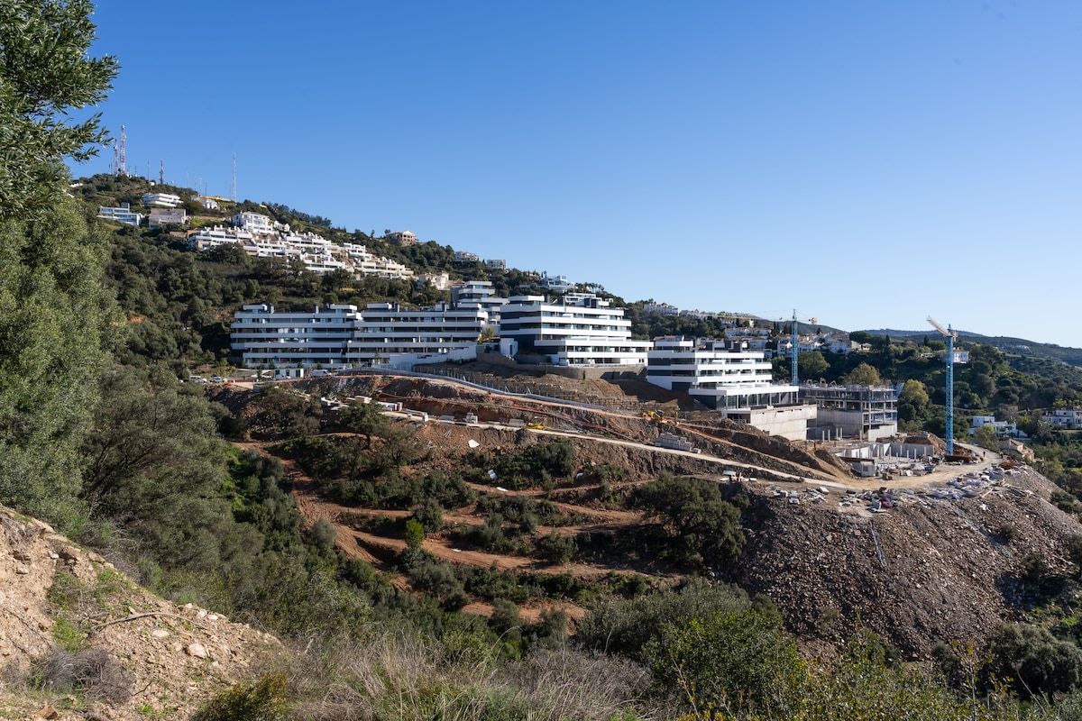 A hillside residential area with modern multi-story buildings, a clear sky, and a construction site.