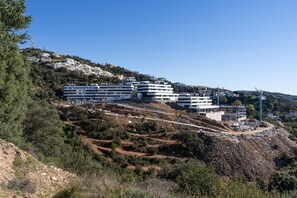 A hillside residential area with modern multi-story buildings, a clear sky, and a construction site. - Med Blue by Time& Home (Marbella)