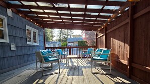 A covered outdoor deck with wooden flooring and metal-framed chairs with cushions. - ​The Seattle Scenes House: 5-Suite Boutique Home near Light Rail (Seattle)