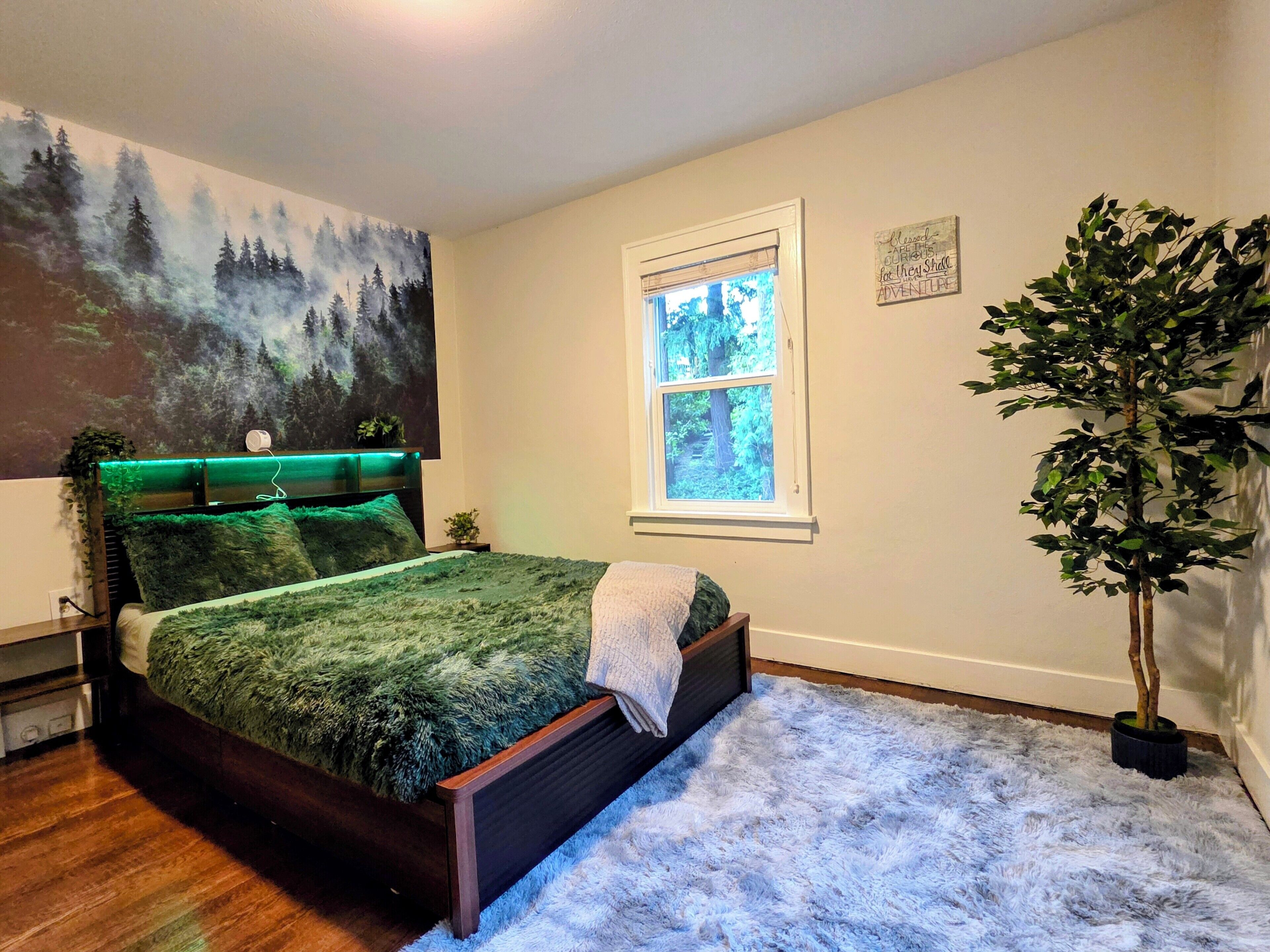 Een slaapkamer met een bed, een raam, een schilderij en een plant.